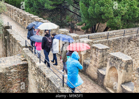 1. März 2018: Lissabon, Portugal - Touristen mit Sonnenschirmen auf den Wällen von Lissabon Kaste, Sightseeing im Regen. Stockfoto