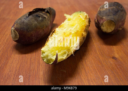Holzkohle gegrillten süsse Kartoffeln, geschält, zwei ungeschält auf hölzernen Hintergrund Stockfoto
