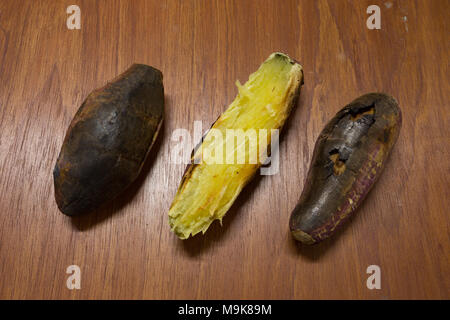 Holzkohle gegrillten süsse Kartoffeln, geschält, zwei ungeschält auf hölzernen Hintergrund Stockfoto