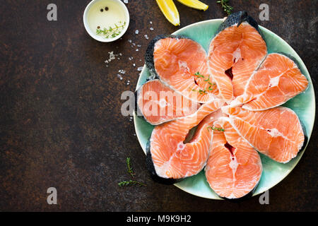 Frischer Lachs und Zutaten zum Kochen (Olivenöl, Zitrone, Gewürze) auf einem dunklen Stein Tabelle. Die richtige Ernährung. Stockfoto