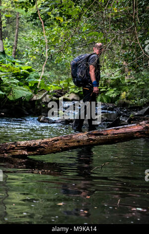 Ein Mann mit Rucksack macht seinen Weg durch den Fluss in einem dichten Wald. Konzept der Exploration und Überleben in der Wildnis. Stockfoto