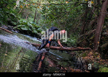 Ein Mann ist das Springen über eine Holz Anmelden beim durchqueren eines Flusses. Konzept des Überlebens in der Wildnis. Mаn vs wild. Stockfoto