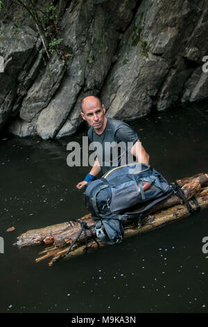 Ein Mann, der seinen Weg durch einen Fluss treibt ein Hand-made Raft log mit seinem Rucksack. Konzept der Exploration und Überleben in der Wildnis. Stockfoto