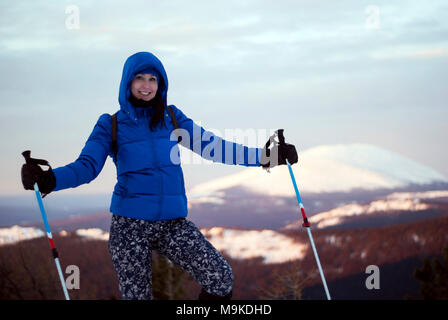 Traveler girl in warme Kleidung mit Stöcke für Nordic Walking in den Händen vor dem Hintergrund einer dawn Winter blurry Berglandschaft Stockfoto