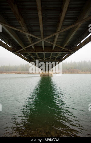 Eine Ansicht von unterhalb der Noxon truss Stahl Brücke über den Clark Fork River auf einem nassen, verschneiten Tag. Stockfoto