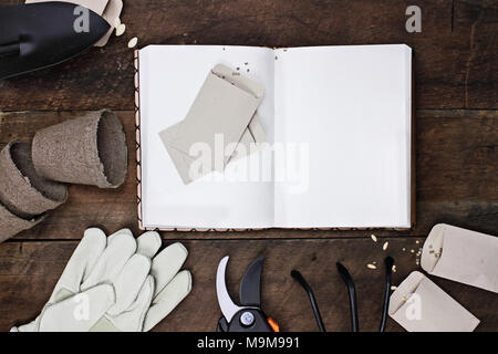 Gartenarbeit Journal mit Tools, Tomatensamen und Blumentöpfe auf einem rustikalen Holztisch umgeben. Bild geschossen von oben im flachen Stil legen. Stockfoto