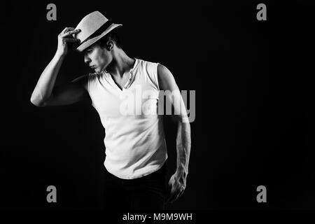Man Fashion Model, stilvolle junge Mann mit Fedora Hut ständigen posiert, über schwarzen Hintergrund. Schwarz-weiß Foto. Stockfoto