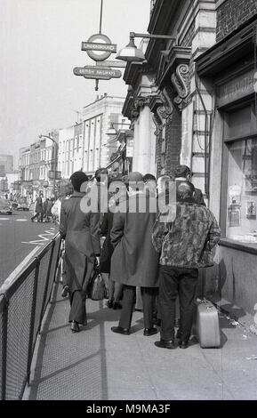 1970 s, historischen, Bahnreisende Schlange auf dem schmalen Bürgersteig außerhalb New Cross Bahnhof in South East London, England. Zu diesem Zeitpunkt, Streiks und abgebrochen Züge wurden ein gemeinsames Auftreten auf der British Rail und in diesem Fall die Plattformen waren zu voll, um mehr Fahrgäste zu nehmen. Stockfoto