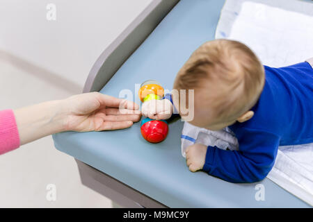 Kind mit Mutter spielt am Wickeltisch. Mom, Spielzeug, baby boy klappern. Blick von oben. Stockfoto