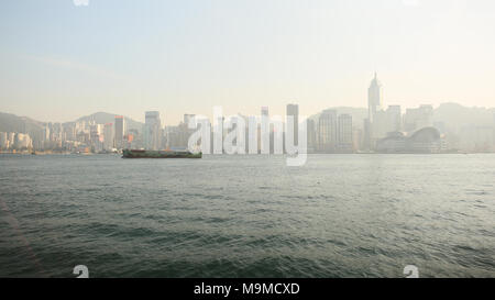 Hongkong, China - Januar 1, 2016: Blick auf die Stadt Hongkong und das Meer mit einem schwimmenden Schiff. Panorama der Stadt am Nachmittag. Architektonische Gebäude im Hintergrund der Berge. Stockfoto