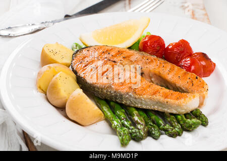 Scheibe der gegrillten Lachs garniert mit gekochten Kartoffeln, grünem Spargel, Sauted Cherry Tomaten und Zitronen Stockfoto