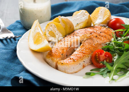 Scheibe der gegrillten Lachs garniert mit gekochten Kartoffeln, Rucola und Cherry Tomaten Salat, Joghurt Sauce mit Kräutern und Zitrone Stockfoto