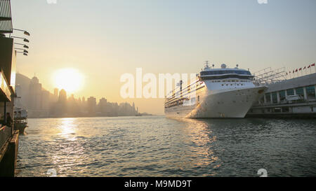 Cruise Liner in Victoria Harbour in den Strahlen der untergehenden Sonne. Blick auf das Meer von Hong Kong und Wolkenkratzer vor dem Hintergrund der Berge. Stockfoto