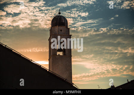 Ein Glockenturm steht hoch über den Dächern der Altstadt Dubrovnik, Kroatien wie der Sonnenuntergang ein blauer himmel orange mit leuchtet. Stockfoto