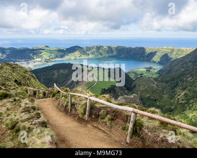 Pfad zu der Straße unten: ein Schmutz weg mit hölzernen Geländer Winde über die Hügel zu einem spektakulären Aussichtspunkt hoch über Sete Cidades und scheint zu einem Straße verbinden weit unten. Stockfoto