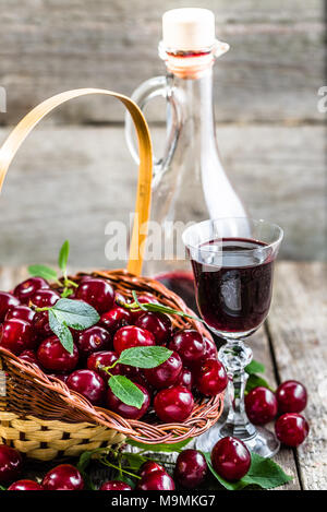 Glas cherry Tinktur, gesunden Alkohol in einer Flasche am rustikalen Holzmöbeln Hintergrund Stockfoto