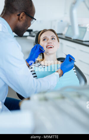 Positive Atmosphäre. Angenehme Patientin lächelte ihr Zahnarzt, während Sie Ihre Zähne gründlich während einer regelmäßigen Überprüfung geprüft Stockfoto