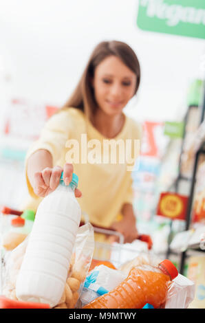 Junge Frau einkaufen im Supermarkt, sie setzen eine Flasche Milch in den Warenkorb Stockfoto