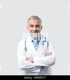 Zuversichtlich reife Arzt posiert mit verschränkten Armen, er lächelt an Kamera Stockfoto