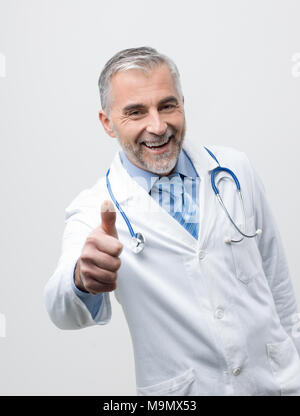 Sicher ein Lächeln auf den Lippen reife Arzt posieren und einen Daumen nach oben Stockfoto