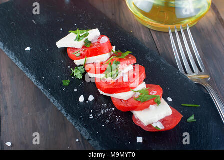 Salat mit Frischkäse und Tomaten auf einen schwarzen Stein. Dunklen alten Holztisch. Stockfoto