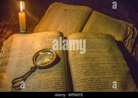 Eine offene alte Gebet Bücher und einer Lupe auf seinem geöffneten Seiten unter dem Licht einer Kerze Stockfoto