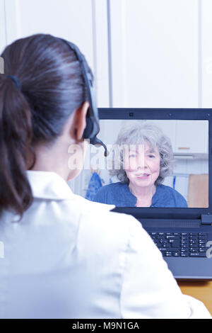 Ärztin für Geriatrie mit Headset vor Ihrem Laptop während einer Konsultation über das Internet mit einem älteren Patienten, Telemedizin Konzept Stockfoto