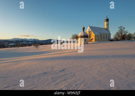 Barocke Wallfahrtskirche Wilparting und Kapelle gegen den blauen Himmel in der schneebedeckten Landschaft glühende in warmes Licht bei Sonnenaufgang, Bayern, Deutschland Stockfoto