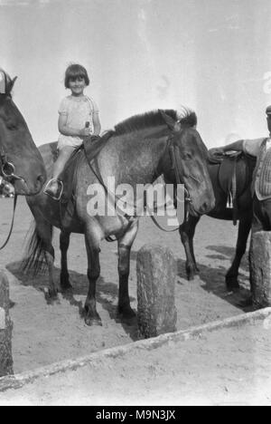 1920s, historische Bild, das ländliche Leben in England, vor der Ankunft auf Masse Der motorcar bedeutete, dass die meisten jungen Leute auf dem Land gelernt, Pferde zu reiten und hier sehen wir ein kleines Mädchen in einem Kleid sitzen bequem auf einem großen Pferd. Stockfoto