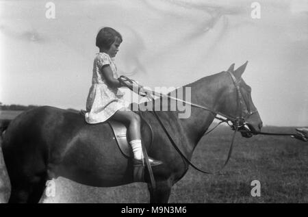 1920s, historische Bild, das ländliche Leben in England, vor der Ankunft auf Masse Der motorcar, dazu geführt, dass die meisten Jugendlichen das Leben auf dem Land gelernt, Pferde von einem frühen Alter zu fahren und hier sehen wir ein junges Mädchen tun genau das. Trägt ein Kleid, sie sitzt auf und halten die Zügel der ein großes Pferd. Stockfoto