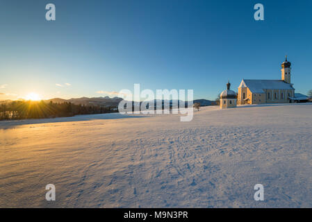 Panorama der barocken Wallfahrtskirche Wilparting und Kapelle gegen den blauen Himmel in verschneiten Alpenlandschaft mit der Sonne bei Sonnenaufgang, Bayern, Deutsch Stockfoto