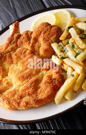 Gebratene Schnitzel Milanese mit Zitrone und Pommes frites Close-up auf einem Teller. Vertikale Stockfoto