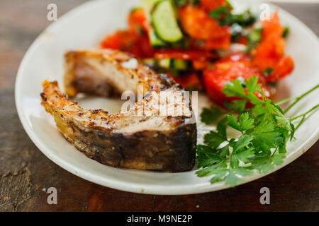 Gebratener Fisch mit Salat auf einem weißen Teller Stockfoto