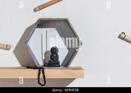 Kleine Statue des Buddha im Rahmen und Rosenkranz auf Holzregal Stockfoto