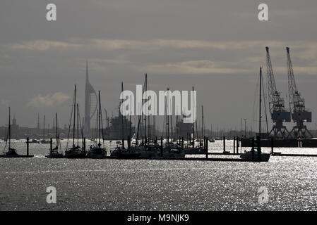 Blick über den Hafen von Portsmouth Fareham Creek Trail mit Yachten im Vordergrund, Marineschiffe, Kräne und die Spinnaker Tower in der Ferne. Stockfoto