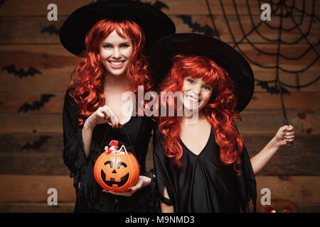 Halloween Konzept - Schönen weißen Mutter und ihre Tochter mit langen roten Haaren in Hexe Kostüme mit Halloween Candy und Zauberstab. Stockfoto