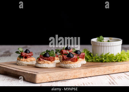 Leckere Häppchen mit Salami, Oliven und Gewürze auf einem waldigen Hintergrund Stockfoto