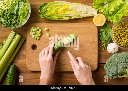 Salat mit frischem Gemüse zubereiten. Schneiden frische Gurke auf einem Schneidebrett. Weibliche Hände. Stockfoto