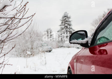 Auf Spiegel der roten Auto auf einer Straße im Winter mit Schnee bedeckt die Landschaft im Hintergrund geparkten Detail. Stockfoto