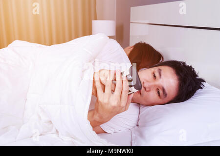 Junger Mann mit seinem Handy im Bett, während seine Frau schläft neben ihm Stockfoto