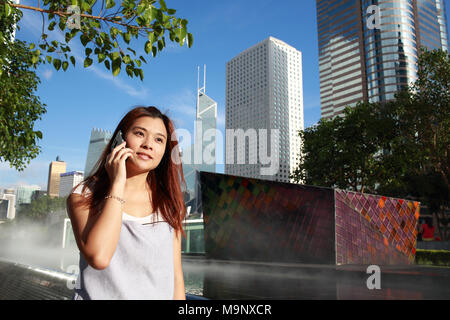 Asiatische Mädchen am Telefon in einer geschäftigen Stadt mit gutem Wetter in Hong Kong Downtown Stockfoto