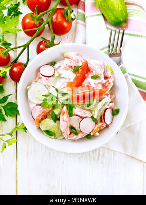 Salat von frischen Tomaten, Gurken und Radieschen mit grünen Zwiebeln und Petersilie, gewürzt mit Mayonnaise und Sauerrahm in eine Schüssel, Handtuch und Gabel auf der Stockfoto