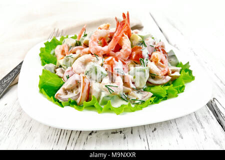 Salat mit Garnelen, Avocados, Tomaten und Mayonnaise auf den grünen Salat auf einen Teller, Servietten, Gabel auf dem Hintergrund der hölzernen Tisch Stockfoto