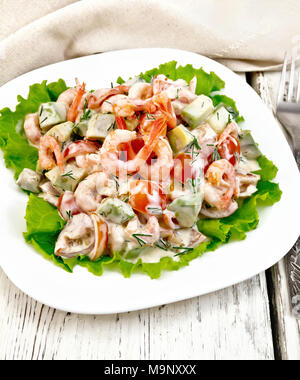 Salat mit Garnelen, Avocados, Tomaten und Mayonnaise auf den grünen Salat auf einen Teller, Servietten, Gabel auf dem Hintergrund der Holzbretter Stockfoto
