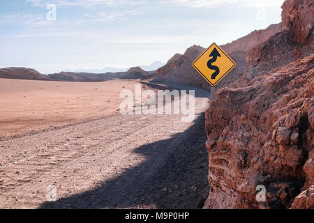 Eine kurvenreiche Straße in einer Wüstenlandschaft mit einem gelben Straßenschild. Stockfoto