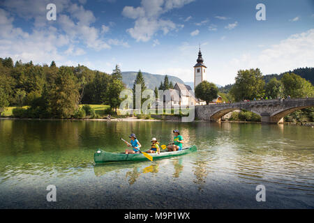 Familie im Kanu auf dem Bohinjer See, mit Kirche und Brücke von Ribcev Laz im Hintergrund, Triglav, Slowenien Stockfoto