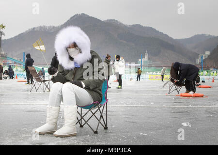 Eine Frau herzlich in einem dicken Fell gekleidet wartet oben ein Loch in das Eis während der Eis angeln Festival an Hwacheon Sancheoneo in der Region Gangwon-do in Südkorea. Die Hwacheon Sancheoneo Ice Festival ist eine Tradition für die Menschen in Korea. Jedes Jahr im Januar Menschenmassen versammeln sich auf dem zugefrorenen Fluss der Kälte und dem Schnee des Winters zu feiern. Hauptattraktion ist Eisfischen. Jung und Alt warten geduldig auf ein kleines Loch im Eis für eine Forelle zu beißen. In zelten Sie können den Fisch vom Grill, nach dem sie gegessen werden. Unter anderem sind Rodeln und Eislaufen. Die in der Nähe Pyeongchang Stockfoto