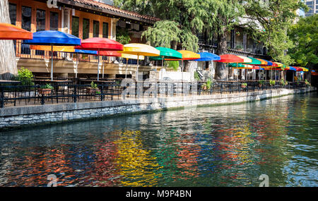 Bunte Sonnenschirme decken Tische in einem Restaurant entlang des San Antonio River Walk auf einer sonnigen Spätsommer Tag. Stockfoto