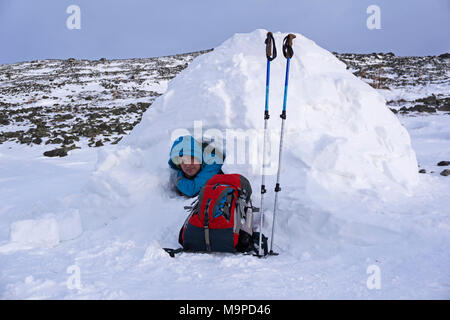 Traveler schaut aus einem verschneiten Haus Iglu vor dem Hintergrund einer Berglandschaft im Winter Stockfoto