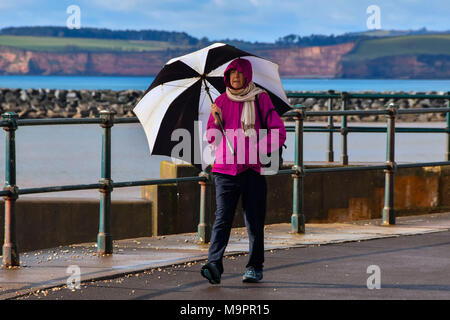 Honiton, Devon, Großbritannien. Am 28. März 2018. UK Wetter. Eine Frau mit einem Regenschirm in einer entlang der Strandpromenade an einem Morgen der sonnigen Perioden in den Badeort Sidmouth Devon Spaziergang nach schweren nächtlichen Regen gelöscht. Foto: Graham Jagd-/Alamy leben Nachrichten Stockfoto